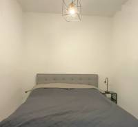 1,5 izb. byt s predzáhradkou, Podunajské Biskupice, projekt Oppidum - Spálňa v 2-izbovom byte so sivou posteľou a závesným svetlom.