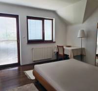 5-izb. dvojpodlažný rodinný dom, Rovinka - Spálňa v rodinnom dome so stolom, postelí a výhľadom cez veľké okná.