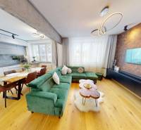 (81 m²) ŠTÝLOVÝ 3i BYT NA SEVERE - Obývacia izba 3-izbového bytu s podlahou s dreveným dekorom, zelenou sedačkou a jedálenským stolom.