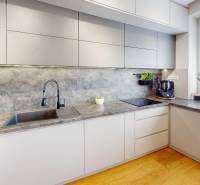 (81 m²) ŠTÝLOVÝ 3i BYT NA SEVERE - Kuchyňa v 3-izbovom byte s modernými bielymi skriňami a podlahou s dreveným dekorom.