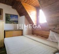 PREDAJ REKREAČNEJ CHATY NA DOMAŠI časť DOBRÁ - Izba v chate s posteľou, drevenými stenami a skrinkou pod šikmým stropom.