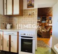 PREDAJ REKREAČNEJ CHATY NA DOMAŠI časť DOBRÁ - Kuchynka v chate so sporákom, keramickým obkladom a prechodom do obývačky s dreveným dekorom.