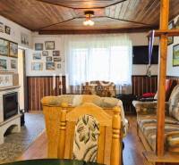 PREDAJ REKREAČNEJ CHATY NA DOMAŠI časť DOBRÁ - Interiér chaty so sedacou súpravou, kachľovou pecou a podlahou s dreveným dekorom.