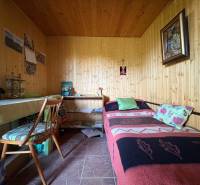 Na predaj: Ovocná záhrada v Leviciach - Drevený interiér s posteľou, stolom a stoličkou v Záhradách.