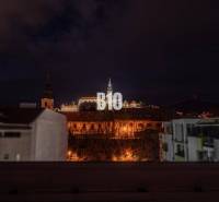 PRIESTRANNÝ Apartmán v CENTRE s výnimočným výhľadom - Nočná scéna Nitry s výhľadom na osvetlený hrad a okolité budovy.