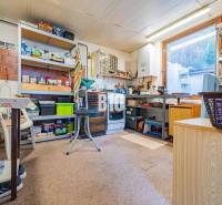 POD HRADOM bývanie alebo podnikanie - Dielňa v rodinnom dome s regálmi, náradím a stolom. V okne je vidieť exteriér.