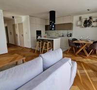 PRENÁJOM - 4 izbový rodinný dom, ktorý je súčasťou dvojdomu   - Obývacia izba v rodinnom dome s podlahou s dreveným dekorom a kuchynským kútom.