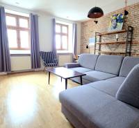 JEDINEČNÝ 2i byt, REKONŠT., 2 X .SAMOST.IZBA, Hviezdoslavovo nám.  - Obývacia izba s tehlovou stenou, sivou sedačkou a podlahou s dreveným dekorom v 2-izbovom byte.
