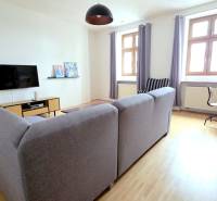 JEDINEČNÝ 2i byt, REKONŠT., 2 X .SAMOST.IZBA, Hviezdoslavovo nám.  - Obývacia izba v 2-izbovom byte so sivou sedačkou a podlahou s dreveným dekorom.