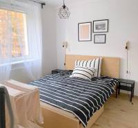 ŠTÝLOVÝ 2i byt, NOVOSTAVBA, BALKÓN, PARKIN, Paričková ulica, NIVY - Izba obsahuje posteľ s pruhovaným obliečkom, biely záves, dekorácie na stene.