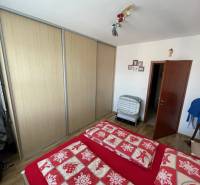 PREDAJ PRIESTRANNÉHO 3 IZB. BYTU NA MUŠKÁTE S GARÁŽOVÝM STÁTIM - Spálňa s podlahou s dreveným dekorom, vstavanou skriňou a červenou posteľnou bielizňou.