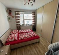 PREDAJ PRIESTRANNÉHO 3 IZB. BYTU NA MUŠKÁTE S GARÁŽOVÝM STÁTIM - Spálňa v 3-izbovom byte s posteľou, skriňou a podlahou s dreveným dekorom.