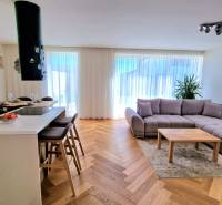 PRENÁJOM - 4 izbový rodinný dom, ktorý je súčasťou dvojdomu   - Obývačka v rodinnom dome s pohovkou, barovými stoličkami a podlahou s dreveným dekorom.