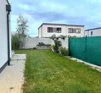 PRENÁJOM - 4 izbový rodinný dom, ktorý je súčasťou dvojdomu   - Dvor rodinného domu v Chorvátskom Grobe s trávnikom a dlažbou, obklopený plotom.