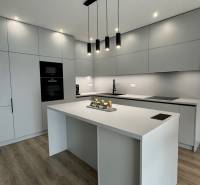 NA PREDAJ 4 izbový rodinný dom Štitáre NITRA - Kuchyňa v rodinnom dome s hladkými sivými linkami a podlahou s dreveným dekorom.