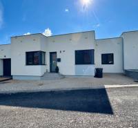 NA PREDAJ 4 izbový rodinný dom Štitáre NITRA - Rodinný dom v Štitároch s bielou fasádou a čiernymi okennými roletami, modrá obloha.