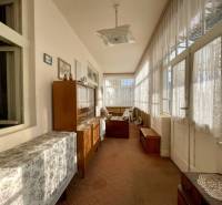 VRAKÚŇ –VEĽKÝ STAVEBNÝ POZEMOK (24 ÁROV) SO STARÝM RODINNÝM DOMOM NA P - Sklenená veranda s čipkovými závesmi a dreveným nábytkom v rodinnom dome.