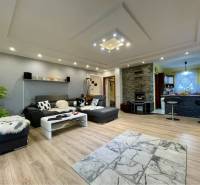 VKUSNÝ 4-IZBOVÝ RODINNÝ DOM S GARÁŽOU NA PREDAJ V OBCI TOPOĽNÍKY - Obývačka v rodinnom dome s rohovou sedačkou, krbom a kuchynským kútom, podlaha s dreveným dekorom.