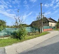 JAHODNÁ – STARÝ RODINNÝ DOM S PEKNÝM STAVEBNÝM POZEMKOM NA PREDAJ - Rodinný dom v Jahodnej s oplotením a stromami popri neuvedenej ulici za slnečného dňa.