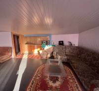 Znížená cena!  Rodinný dom s vnútorným aj vonkajším bazénom na krásne  - Obývacia izba s kobercami, sedačkou a malou kuchynkou v rodinnom dome na ulici.