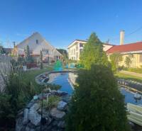 Znížená cena!  Rodinný dom s vnútorným aj vonkajším bazénom na krásne  - Záhrada na ulici, rodinný dom, trávnik s jazierkom a ozdobnými rastlinami.