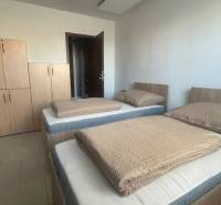 Apartmány na prenájom. - Spálňa s dvomi posteľami a skriňou v bledých odtieňoch v útulnej budove.