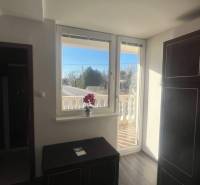 Apartmány na prenájom. - Izba s oknom na balkón, skrinka, cesta vonku, kvety a budova.