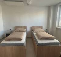 Apartmány na prenájom. - Dve jednolôžkové postele umiestnené v izbe s bielymi stenami a oknom.