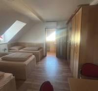 Apartmány na prenájom. - Miestnosť so šikmým stropom, posteľami, skriňou, drevenými podlahami a chodbou.