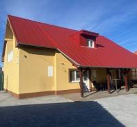 Apartmány na prenájom. - Rodinný dom s červenou strechou a terasou, popisuje vidiecke prostredie a budovu.