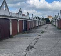 Garáž na prenájom v centre mesta. - Riad garáží s hnedými dverami, nad nimi trojuholníkové strechy pod modrou oblohou.