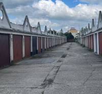 Garáž na prenájom v centre mesta. - Radu garáží tvorí ulica pod modrou oblohou s oblakmi.