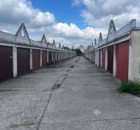 Garáž na prenájom v centre mesta. - Riadok garáží s červenými dverami na dlhej betónovej ceste pod oblohou.