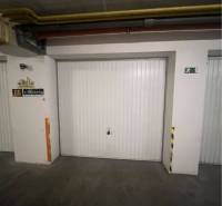Garáž na prenájom. - Uzavreté garážové dvere v budove s osvetlením a bezpečnostným značením.