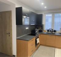 Na predaj: 3-izbový rodinný dom na predaj v obci Lesné Kračany - Kuchyňa v rodinnom dome s čiernymi skrinkami a podlahou s dreveným dekorom.