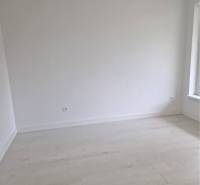 NOVOSTAVBA! Krásny, moderný a priestranný 3-izbový byt s veľkou logiou - Prázdna miestnosť s bielymi stenami a podlahou s dreveným dekorom v 3-izbovom byte.