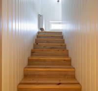 Dvojpodlažný rodinný dom s veľkým pozemkom na predaj v obci Jahodná - Drevené schody vedú na poschodie, svetlé steny rodinného domu osvetľuje okno.