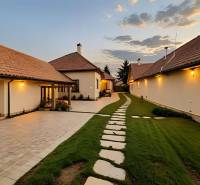 Znížená Cena!Na predaj rodinný dom vo Vrakúni, blízko Dunajskej Stredy - Rodinný dom vo Vrakúni s osvetleným dvorom a kamenistou cestou pri západe slnka.