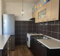 Štartovací 2-izbový byt s balkónom a klimatizáciou – Ohrady - Kuchyňa v 2-izbovom byte s tmavými skrinkami a podlahou s dreveným dekorom.