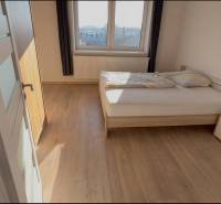 Prenájom 2-izbového bytu, Dunajská Streda - Spálňa v 2-izbovom byte s posteľou, nočným stolíkom a podlahou s dreveným dekorom.