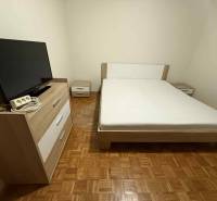Prenájom 3-izbového bytu, Dunajská Streda - Spálňa v 3-izbovom byte s TV, posteľou a nábytkom na podlahe s dreveným dekorom.
