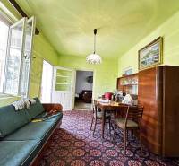 ☎️ 0918197701- Na predaj starší rodinný dom vhodný na kompletnú presta - Obývacia izba rodinného domu s gaučom, jedálenským stolom a sklenenou vitrínou.