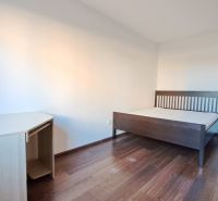 Bývanie s vlastnou predzáhradkou – zariadený 2-izbový byt (62+33 m²) - Spálňa v 2-izbovom byte: posteľ, stôl, podlaha s dreveným dekorom.