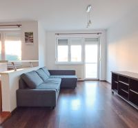 Bývanie s vlastnou predzáhradkou – zariadený 2-izbový byt (62+33 m²) - Obývacia izba v 2-izbovom byte s pohovkou, podlaha s dreveným dekorom a svetlom.