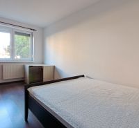 Bývanie s vlastnou predzáhradkou – zariadený 2-izbový byt (62+33 m²) - Spálňa v 2-izbovom byte s podlahou s dreveným dekorom, jednoduchý nábytok a veľké okno.