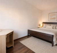 Bývanie s vlastnou predzáhradkou – zariadený 2-izbový byt (62+33 m²) - Svetlá spálňa s posteľou a stolom, podlaha s dreveným dekorom, 2-izbový byt.