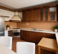 Bývanie s vlastnou predzáhradkou – zariadený 2-izbový byt (62+33 m²) - Kuchyňa s hnedými skrinkami, rohovou linkou a svetlým stolom v 2-izbovom byte.