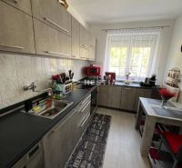 NOVINKA Priestranný 3-izbový byt (99 m²) s pozemkom, terasou, 2 balkón - Kuchyňa s kuchynskou linkou, stolom a podlahou s dreveným dekorom v 3-izbovom byte.