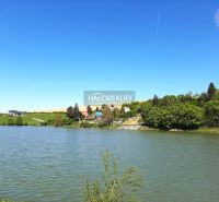 Predaj, záhradný pozemok   1050 m2 Hubina, neďaleko ... - Vodná plocha a domy v okolí záhrad v Hubine, obklopené zeleňou a modrou oblohou.
