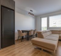 Moderný 2-izbový byt s balkónom, Ovocné sady - Obývačka s koženou sedačkou, jedálenským stolom a podlahou s dreveným dekorom v 2-izbovom byte.